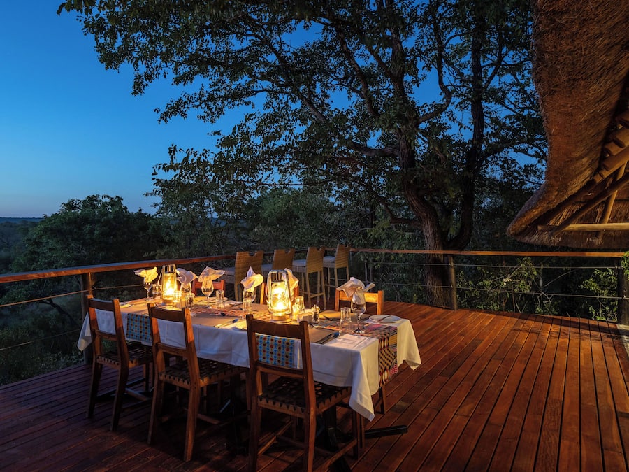 A wooden deck with a table set for dining, surrounded by chairs, and overlooking a natural landscape.