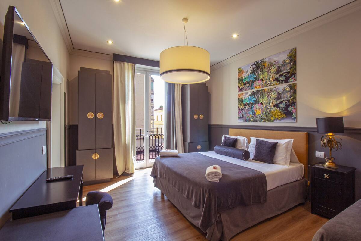 A modern hotel room with a large bed, a desk, a wardrobe, and a balcony with a view.
