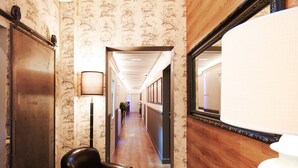 A hallway with patterned wallpaper, a black leather chair, a white lamp, and a mirror on the wall. - Boutique Hotel Hugo (Florence)