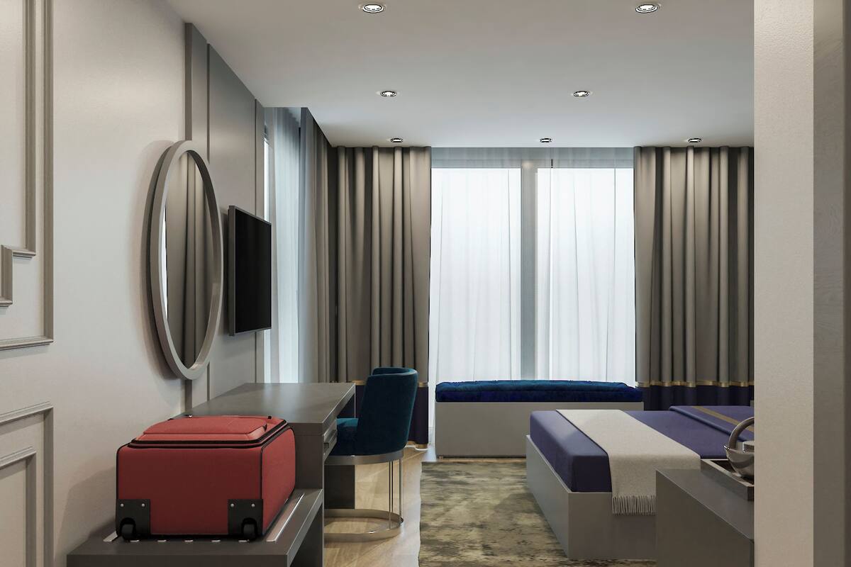 A modern hotel room with a desk, chair, bed, and a red suitcase.