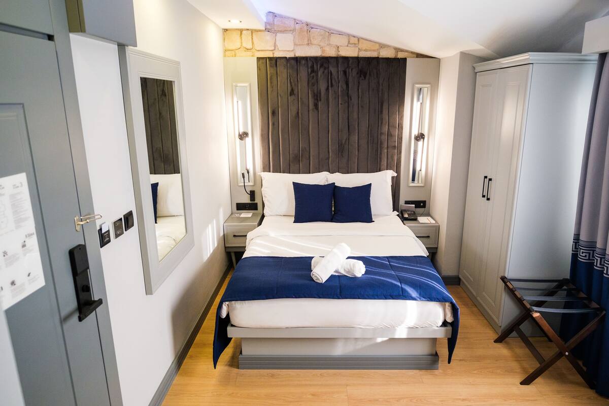 A hotel room with a bed, a desk, a wardrobe, and a mirror.