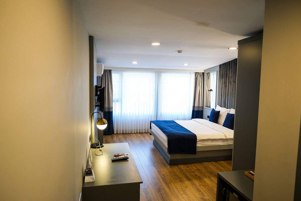 A hotel room with a bed, a desk, a lamp, and a window with curtains.