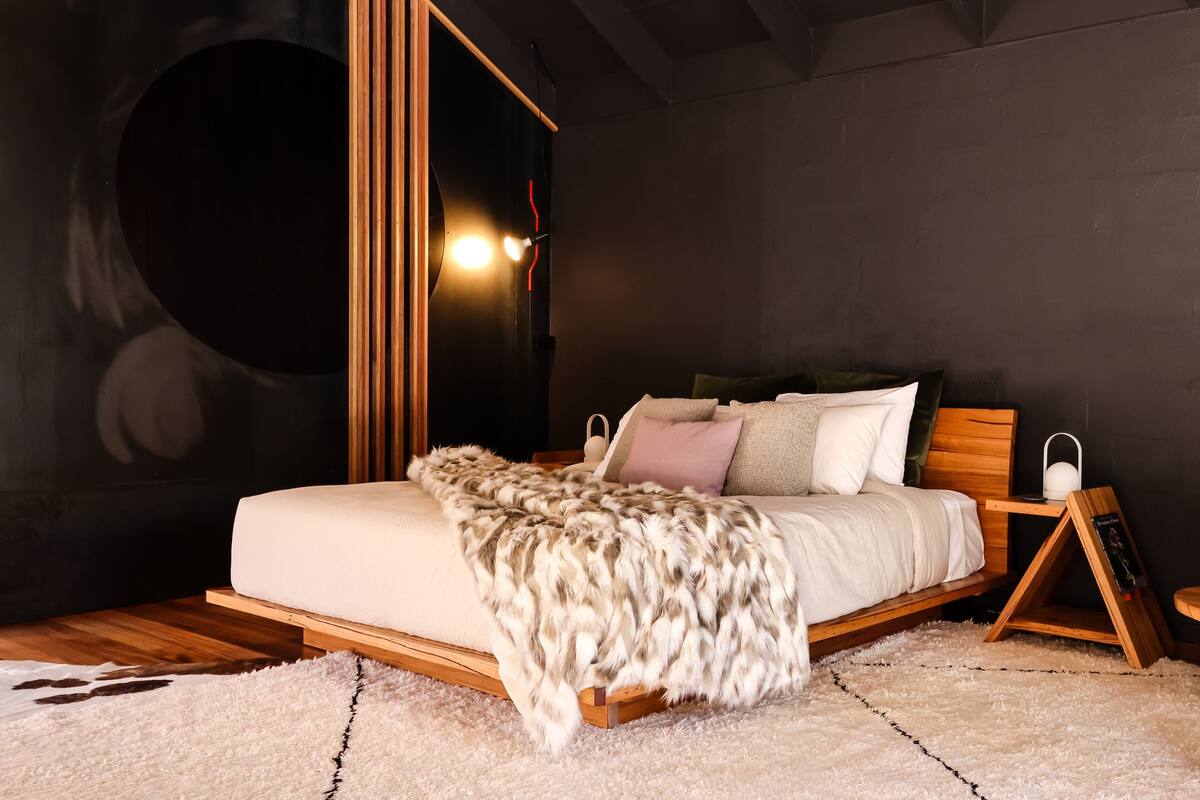 A modern bedroom with a large bed, wooden headboard, and a fluffy white throw blanket.