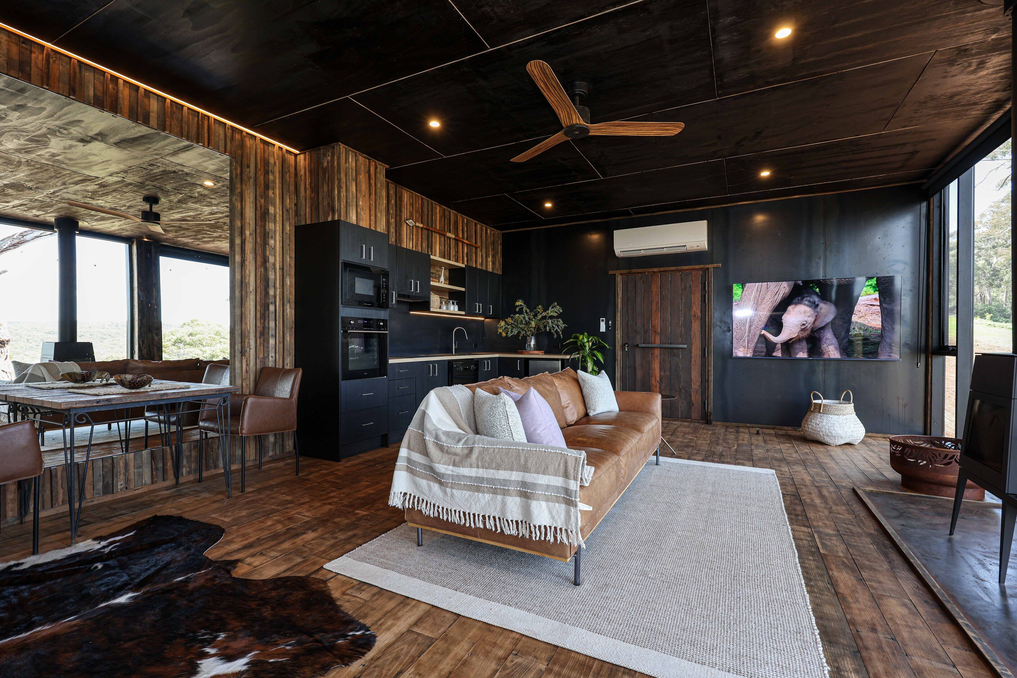 A modern living room with a leather sofa, wooden flooring, and a ceiling fan.