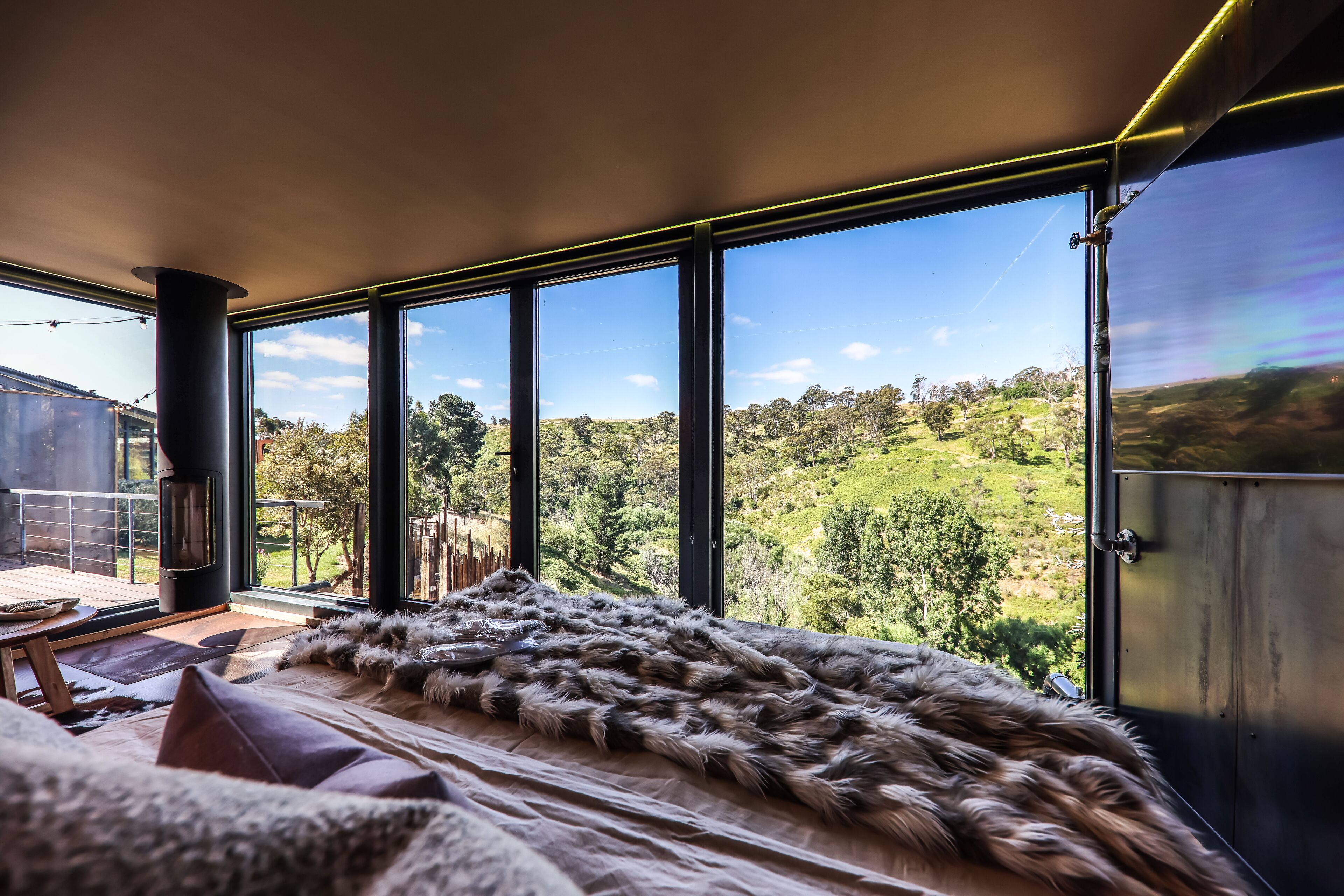 A modern room with large windows, a fur throw, and a view of a green landscape.