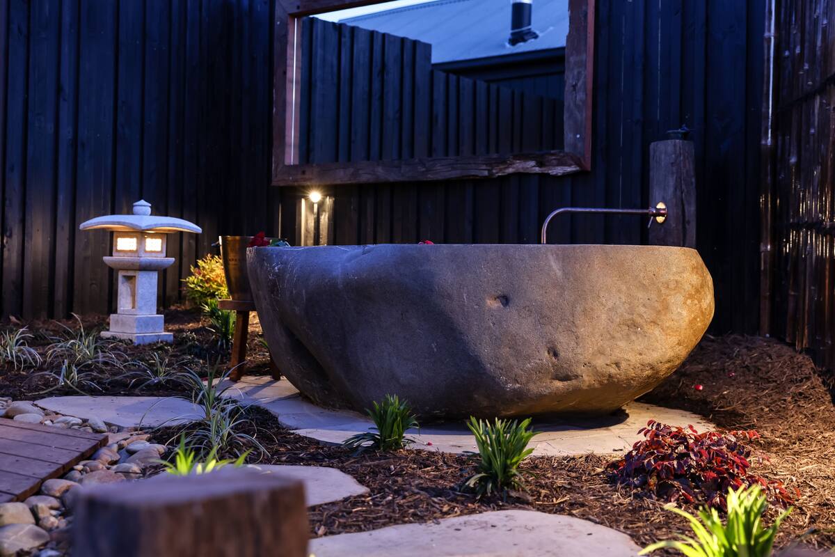 A stone bathtub in a garden with a wooden fence, a stone lantern, and small plants.