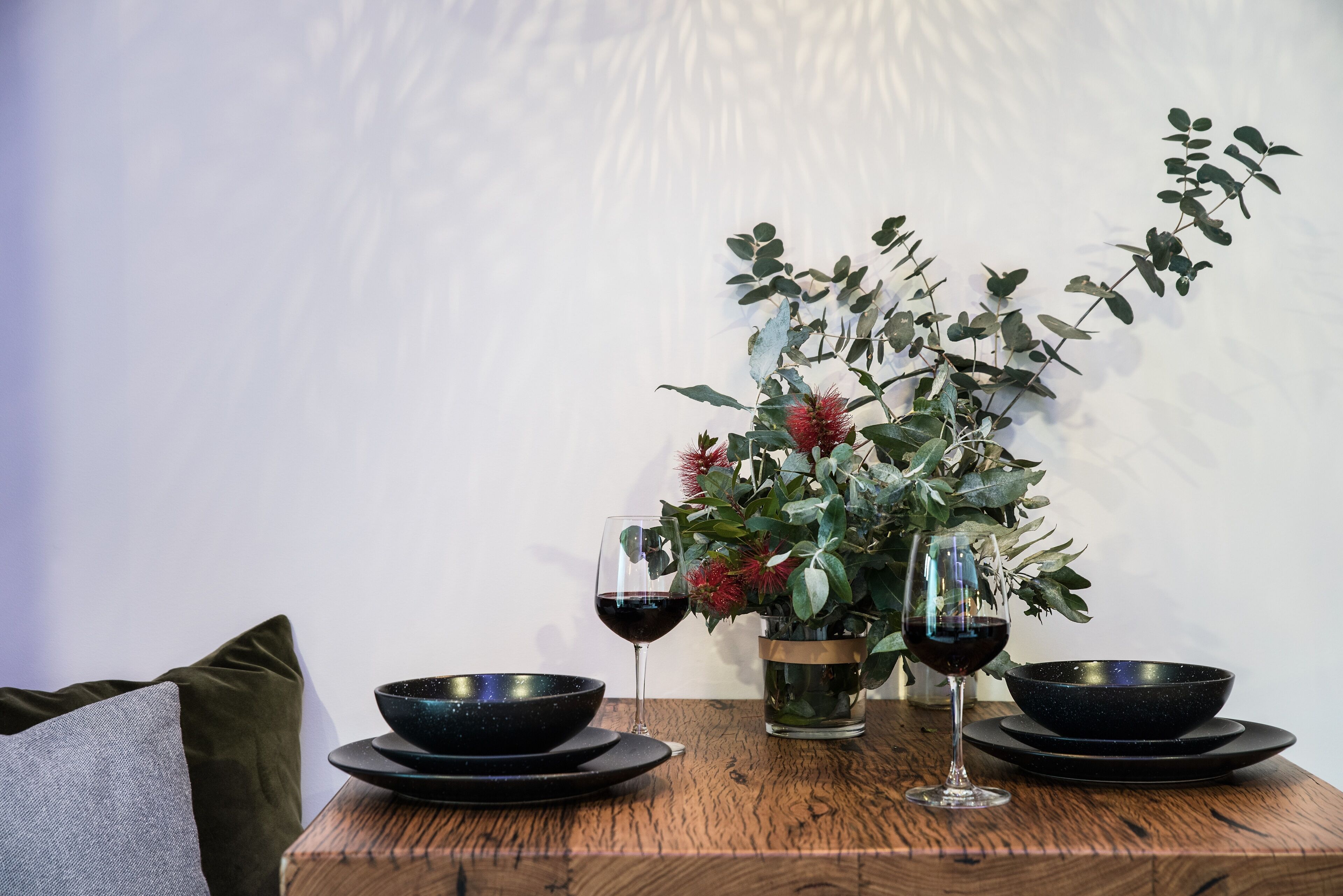 A dining table with black bowls, wine glasses, and a potted plant.