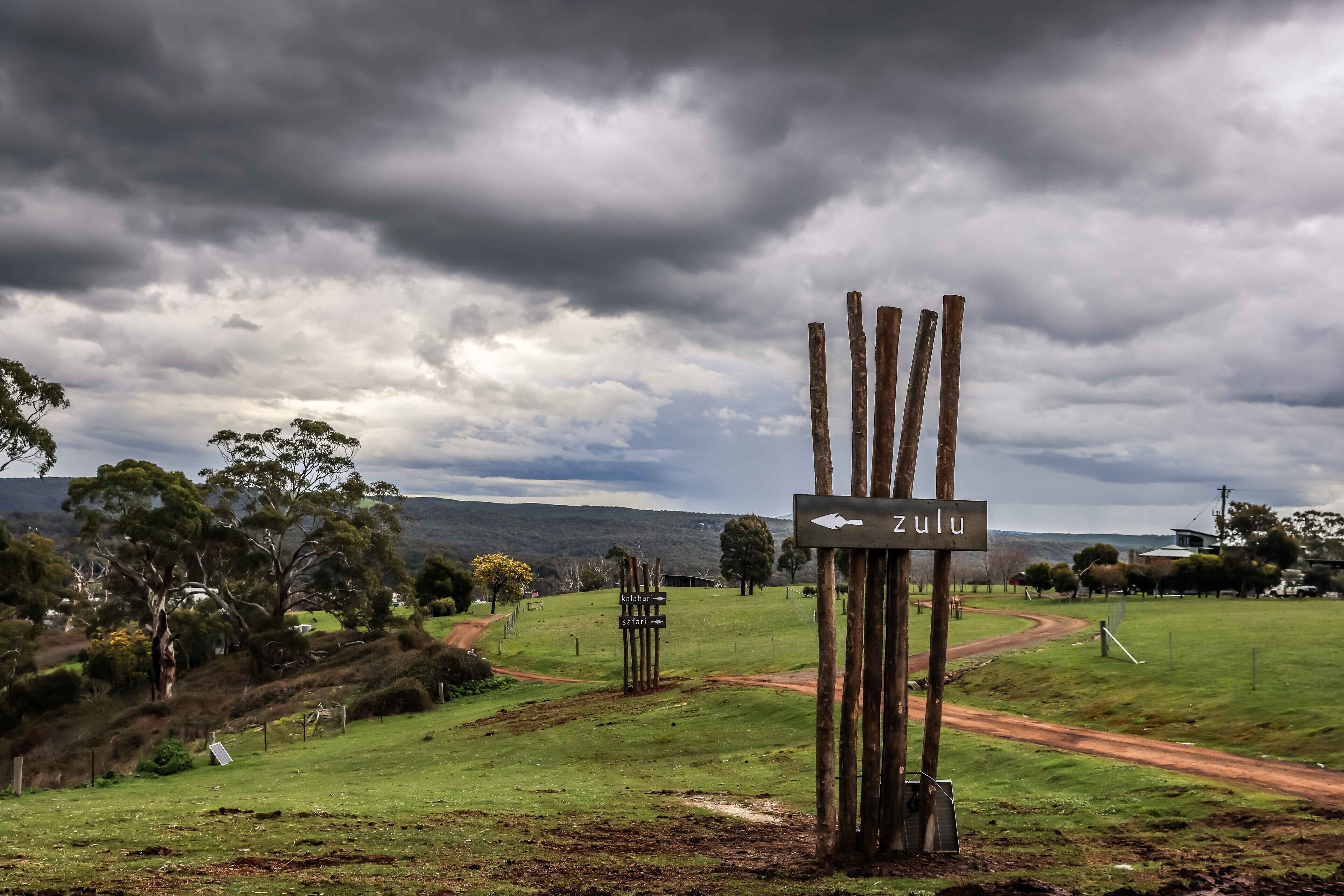 A rural landscape with a wooden signpost indicating directions to Zululand, Kalahari, and Savanna.