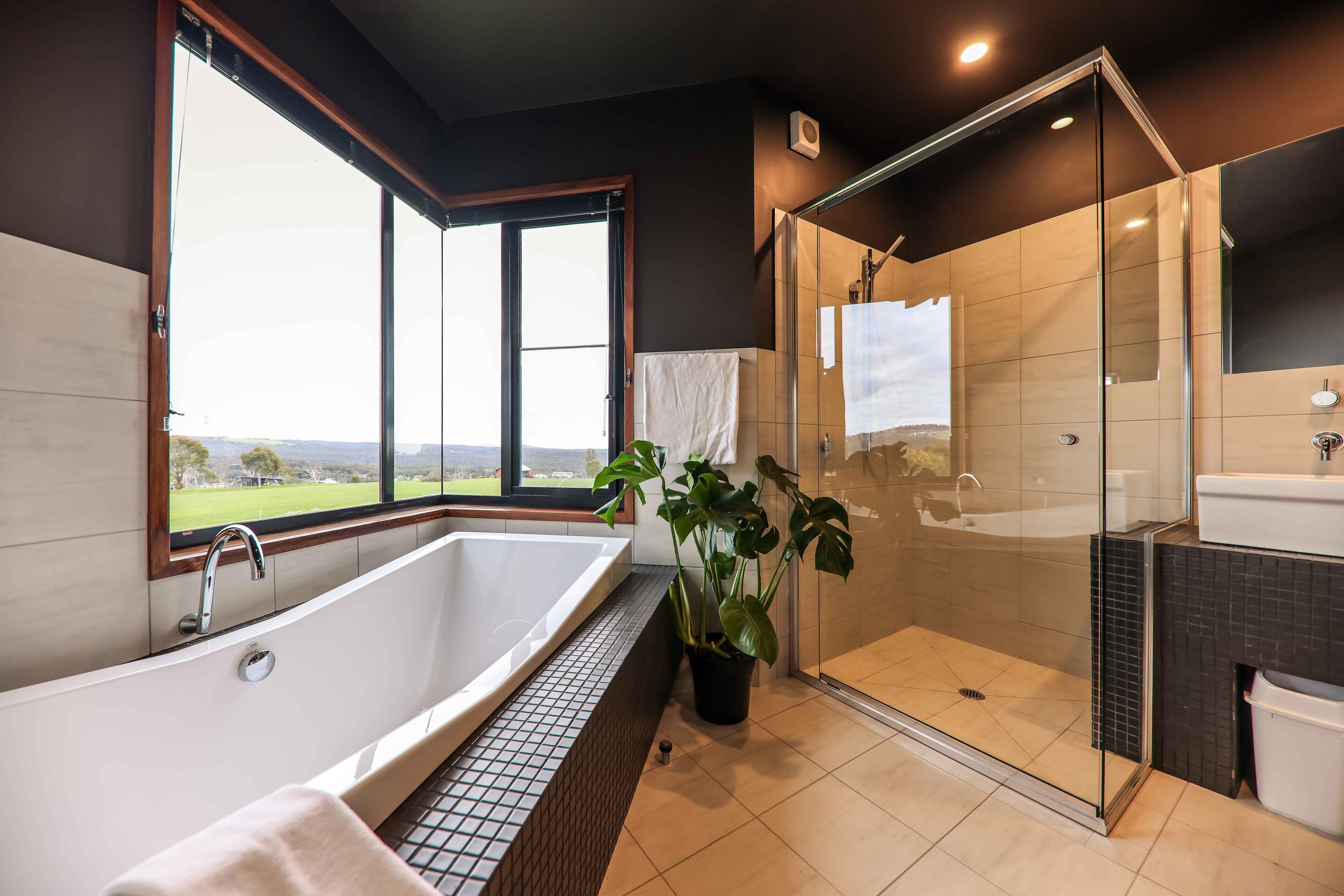 Une salle de bain moderne dotée d’une grande baignoire, d’une douche à parois de verre et offrant une vue sur l’extérieur.