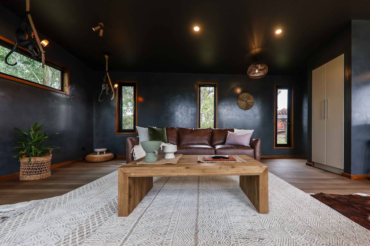 A modern living room with a dark wall, leather sofa, wooden coffee table, and a large window.