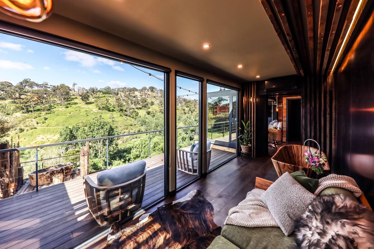 A spacious balcony with a wooden deck, a sofa, and a dining area with chairs.