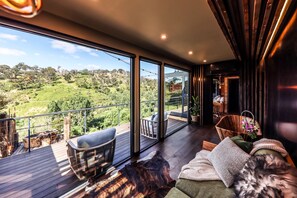 A spacious balcony with a wooden deck, a sofa, and a dining area with chairs. - Clifftop at Hepburn (Hepburn)