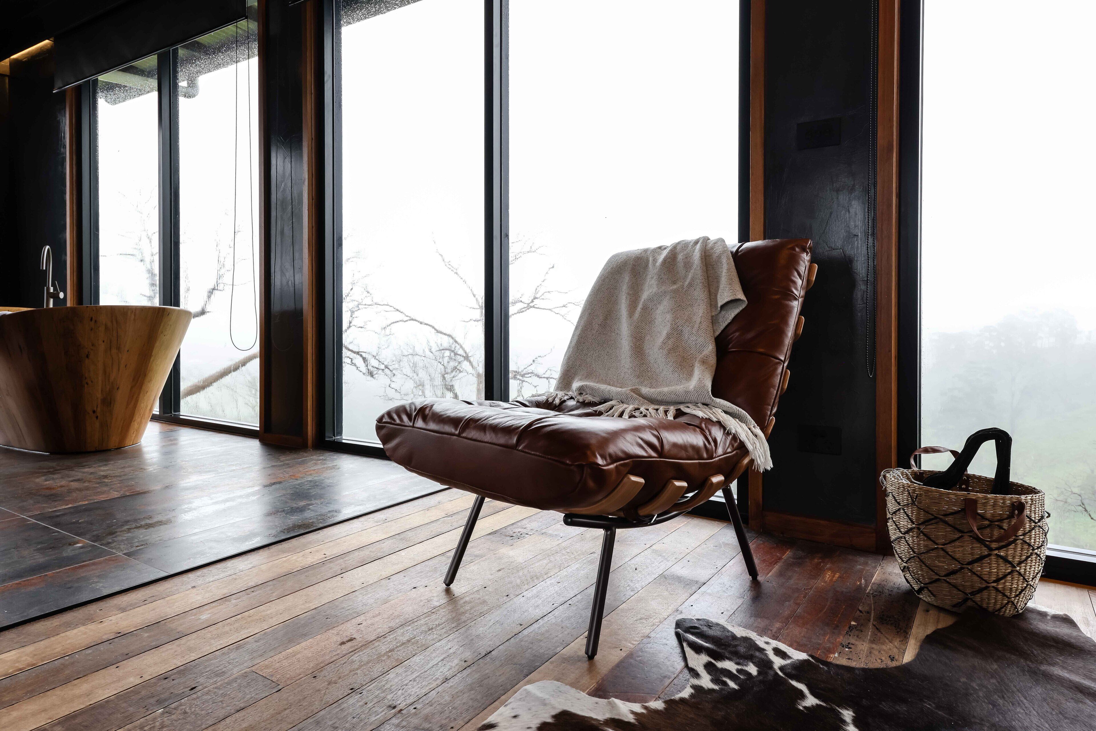 A modern room with a leather chair, a wooden bowl-shaped sink, and a woven basket.