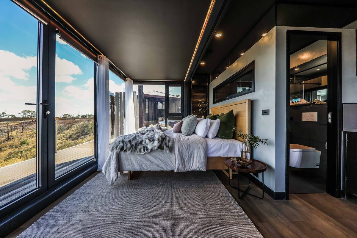 A modern bedroom with a large bed, a view of the countryside, and a minimalist bathroom.