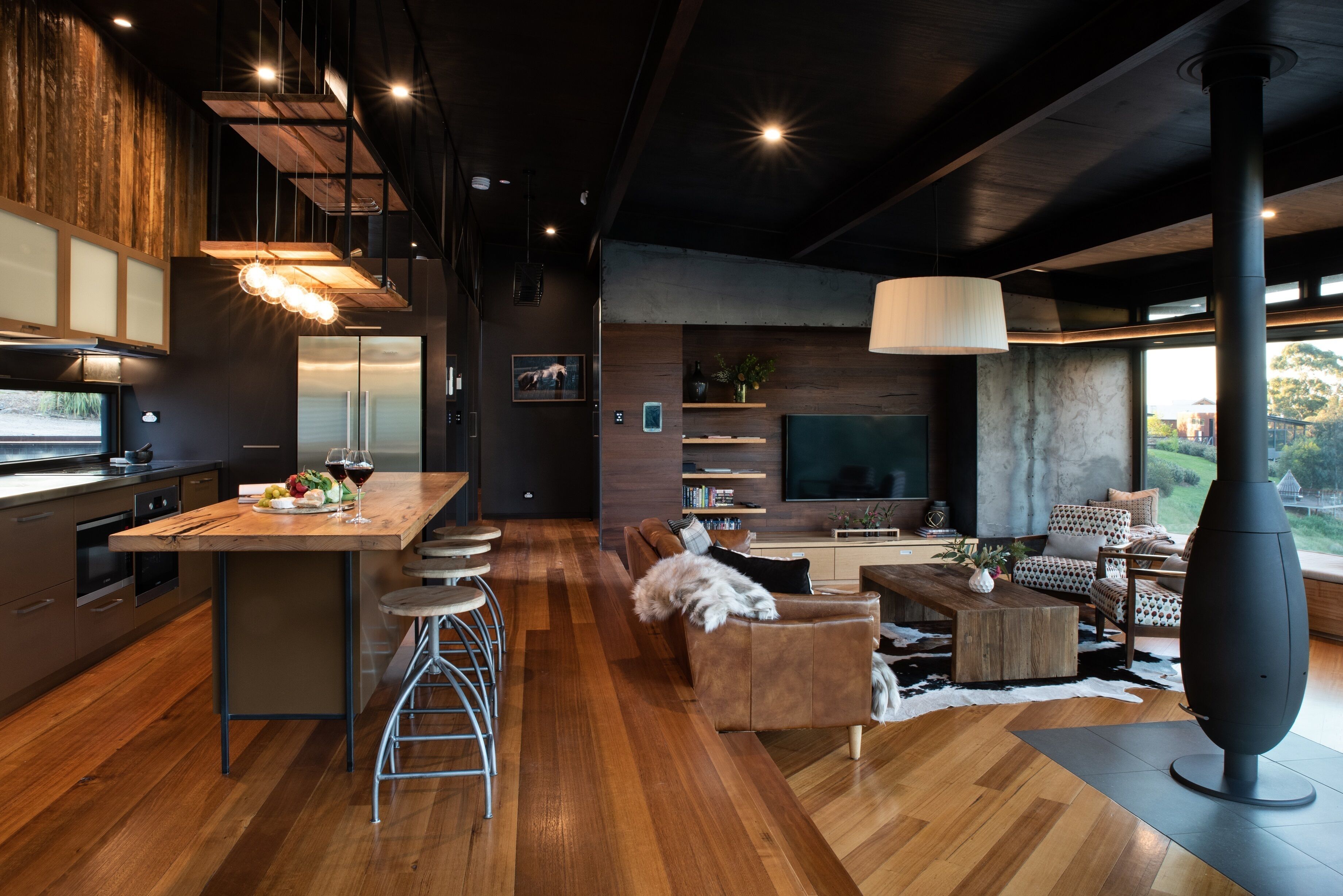 A modern kitchen with a wooden island, bar stools, and a dining area with a sofa and coffee table.
