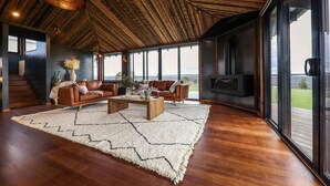 Un salon spacieux doté d’un plafond en bois, de grandes fenêtres, d’une cheminée et d’un ensemble de meubles de salon modernes.
