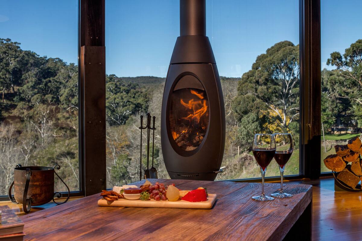 A rustic wooden table with a wood stove, a glass of red wine, and a plate of cheese and grapes.