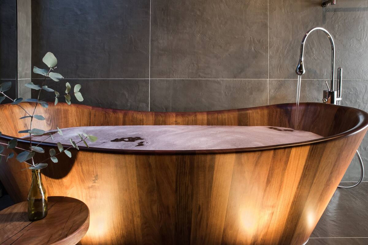 A wooden bathtub with a faucet and a plant on a wooden stool.