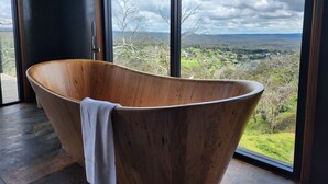 Une baignoire en bois, une serviette, de grandes fenêtres et une vue sur un paysage.