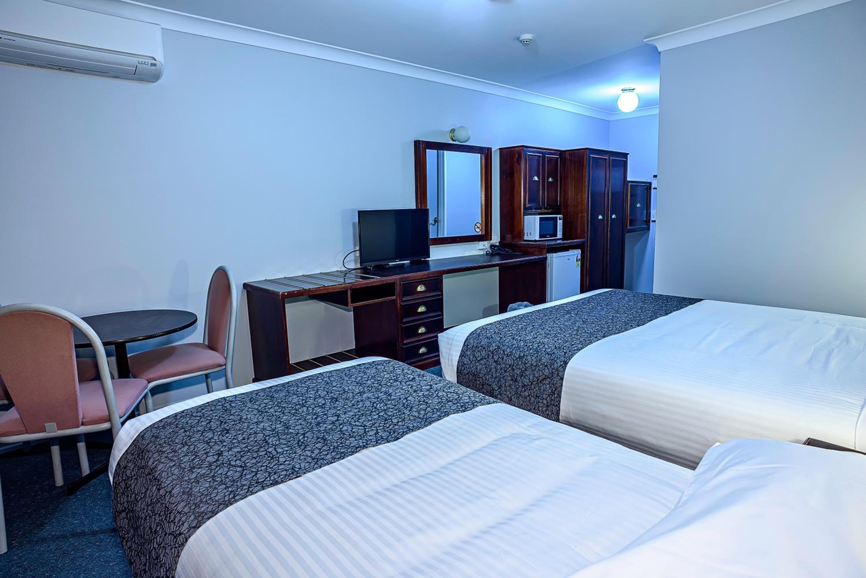 A hotel room with two beds, a desk with a computer, a chair, a small table, and a microwave.