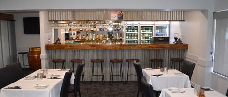 Un restaurante con zona de bar, varias mesas y sillas.