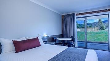 A hotel room with a bed, a small table with chairs, and a view of a grassy area through a glass door.