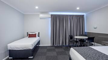 A hotel room with a single bed, a smaller bed, a desk with chairs, and a large window with curtains.