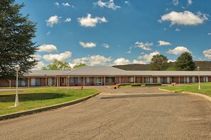 A motel with a long row of rooms, a parking lot, and a grassy area with a lamp post. - Bushmans Motor Inn (Marrangaroo)