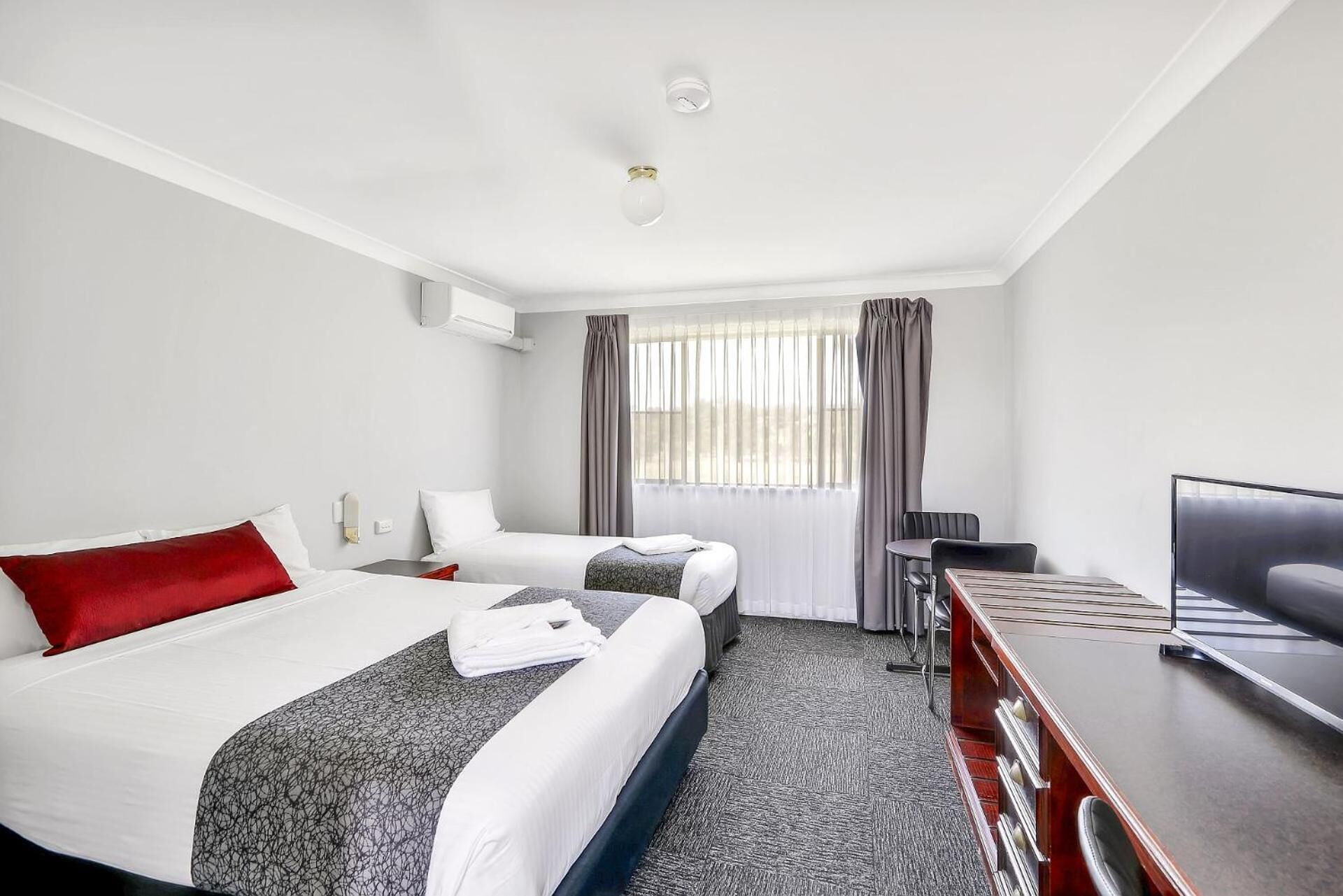 Ein Hotelzimmer mit zwei Betten, einem Schreibtisch, einem Stuhl und einem Fernseher.