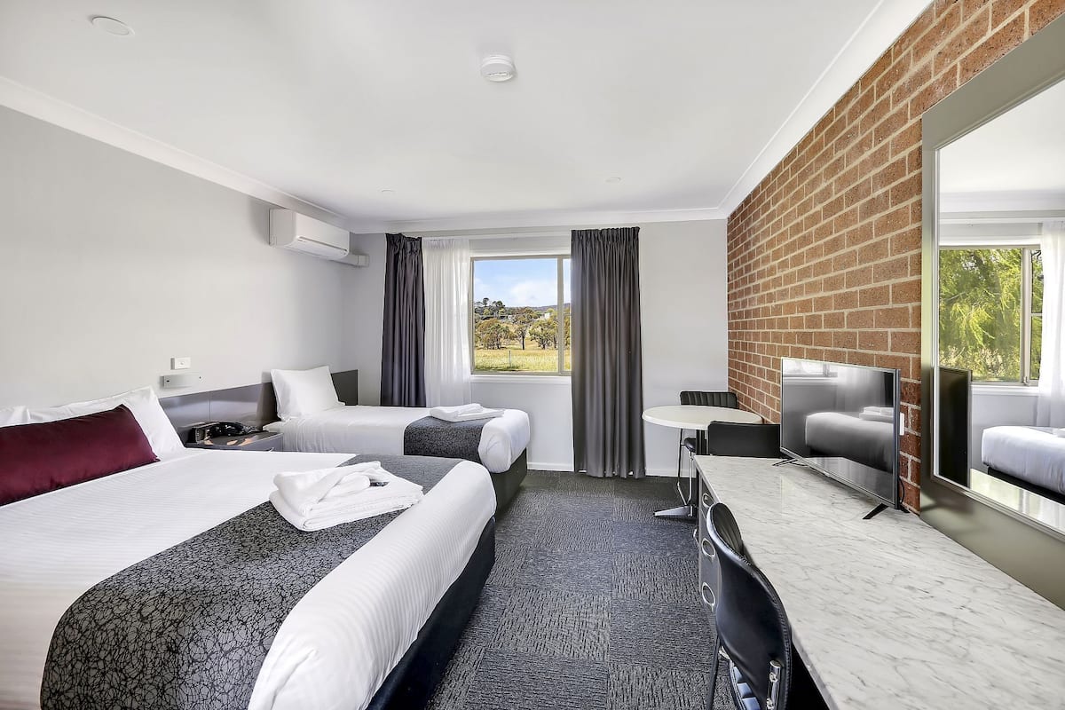 Habitación de hotel con dos camas, un escritorio, una silla, un televisor y un ventanal con vistas al exterior.