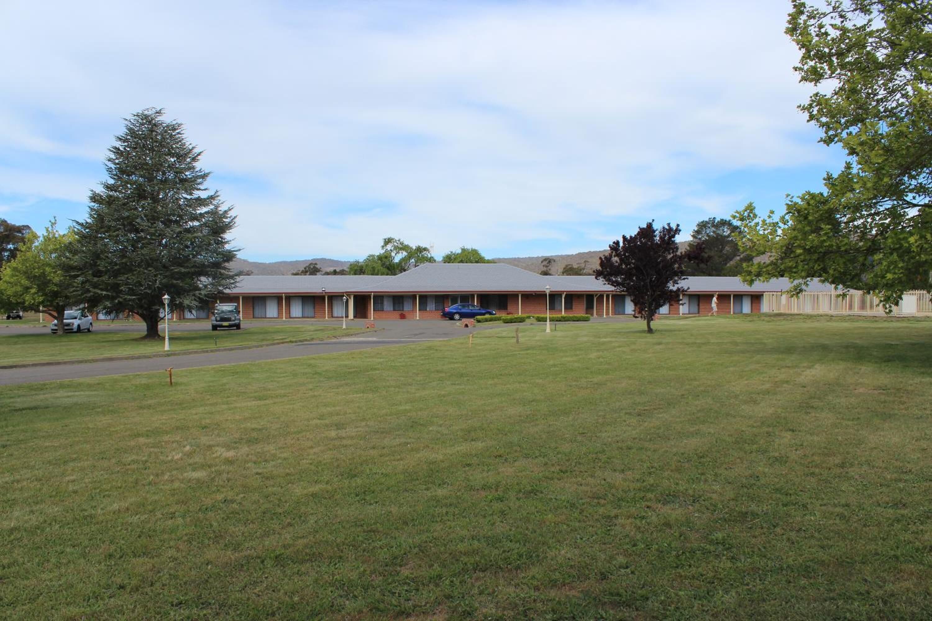 A motel with a row of rooms, a parking lot, and a grassy area.