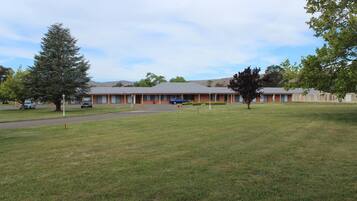 A motel with a row of rooms, a parking lot, and a grassy area.