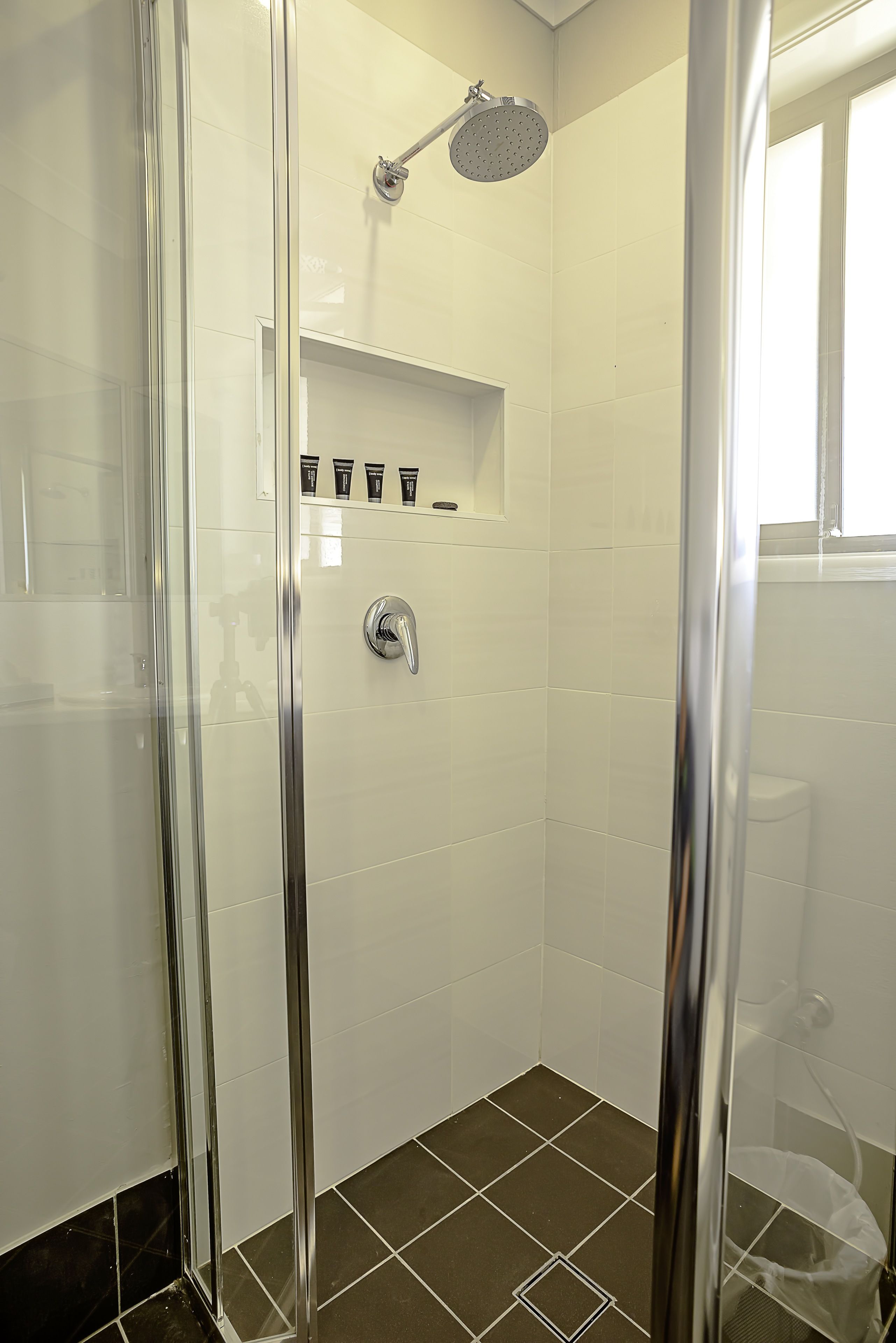 A modern shower with a glass door, a handheld showerhead, and a shelf with toiletries.