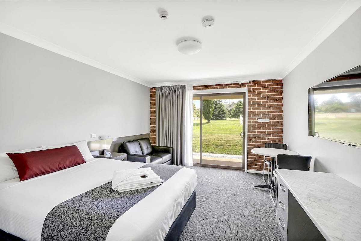 Habitación de hotel con cama, escritorio, silla, una mesita y vistas al exterior.