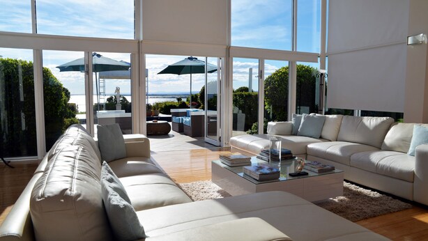A spacious living area with a large window, a sofa, a coffee table, and outdoor furniture. - Tintagel (Metung)