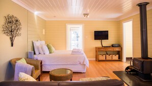 A cozy room with a bed, a television, a fireplace, and a wicker chair. - Avalon Private Spa Villa - Adults Only (Elevated Plains)