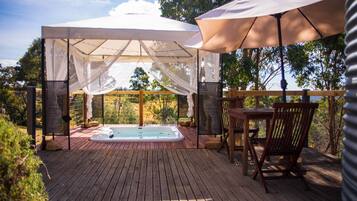 A wooden deck with a hot tub, a covered seating area, and outdoor furniture.