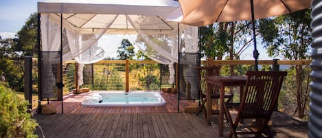 A wooden deck with a hot tub, a covered seating area, and outdoor furniture.