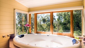 A large oval hot tub in a room with wooden windows and a view of greenery outside. - Avalon Private Spa Villa - Adults Only (Elevated Plains)