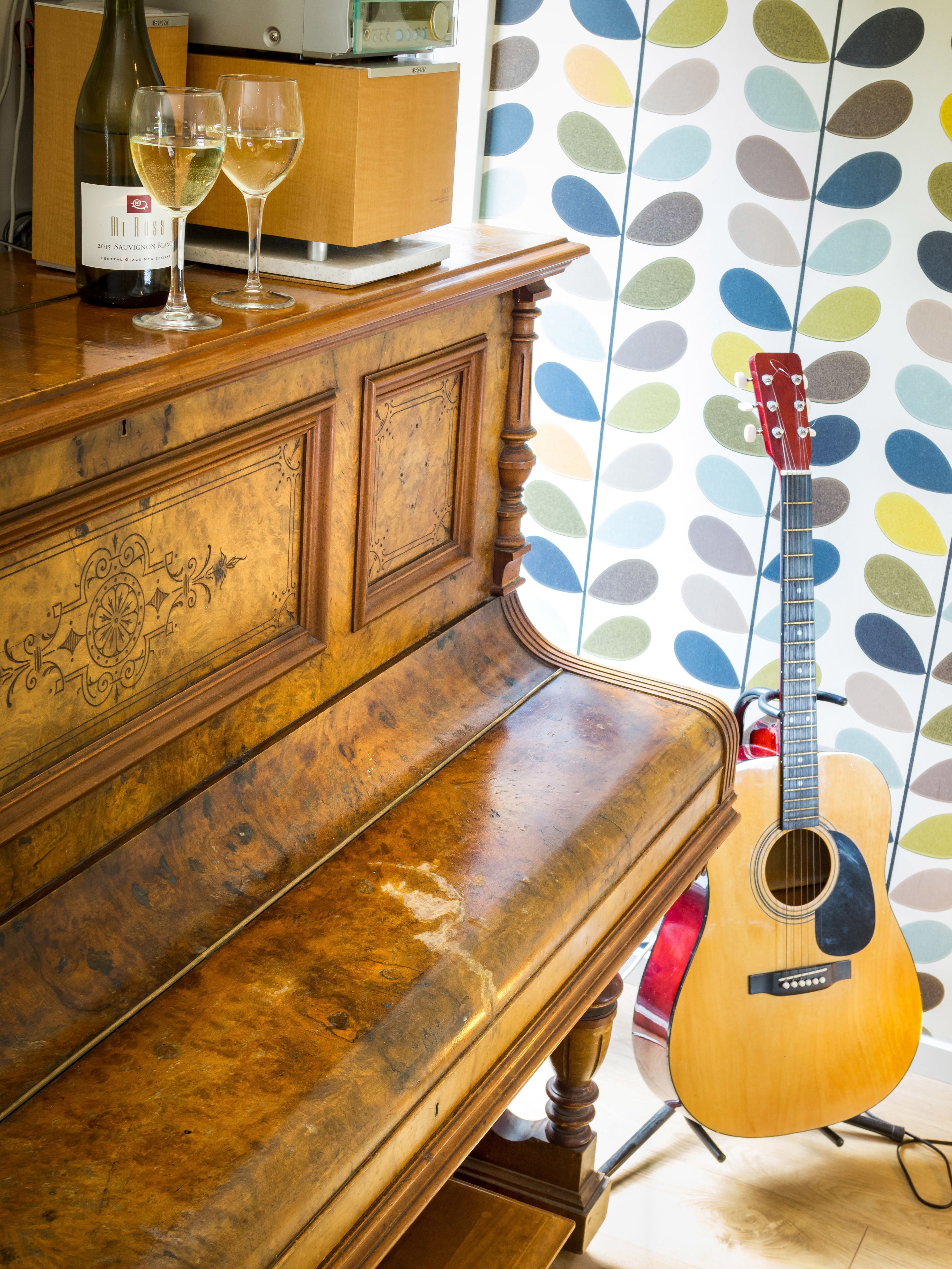 A wooden piano with a guitar leaning against it, and two glasses of white wine on top.