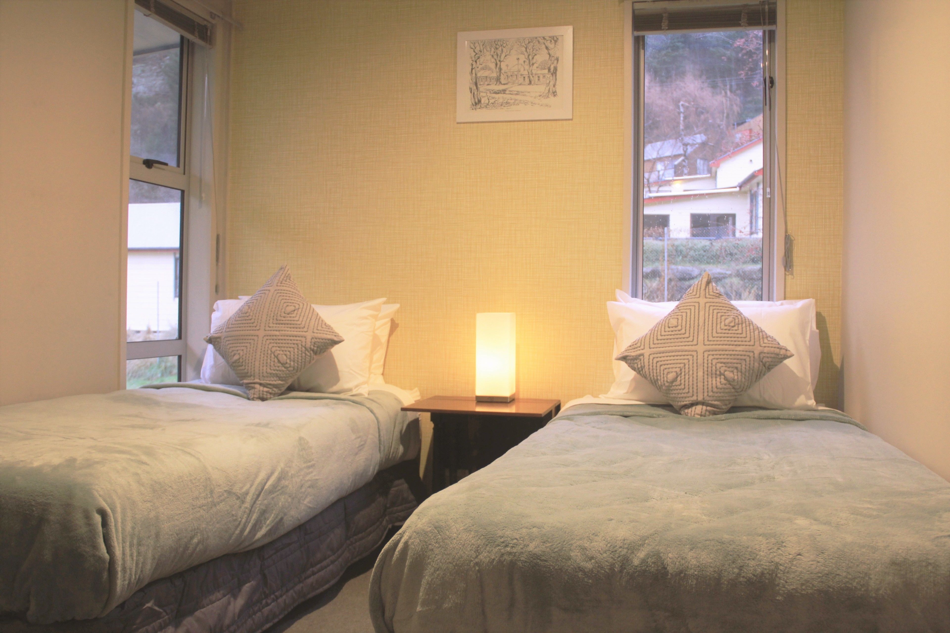 A room with two beds, each with patterned pillows and a bedside table with a lamp.