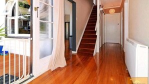 A hallway with wooden flooring, a staircase, and a door leading to another room. - Outdoor Living in Christchurch (Christchurch)
