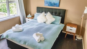 A neatly made bed with blue bedding and white towels, a bedside table with a lamp, and a painting on the wall. - Outdoor Living in Christchurch (Christchurch)
