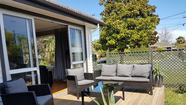 A deck with wicker furniture, a potted plant, and a view of a house with sliding glass doors. - Outdoor Living in Christchurch (Christchurch)