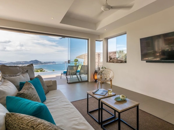 A modern living room with a large sofa, a coffee table, and a view of the sea.