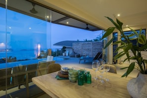 A dining area with a view of the sea, a table set with plates, glasses, and green bottles.