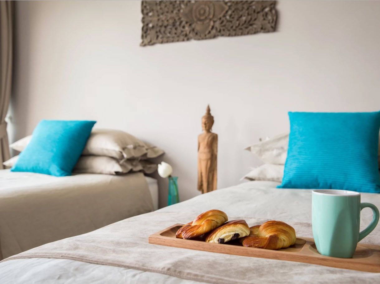 A hotel room with a bed, a wooden tray with pastries, and a mug.