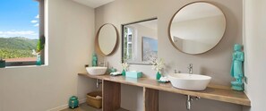 A bathroom with two sinks, a large mirror, and a window with a view of hills.