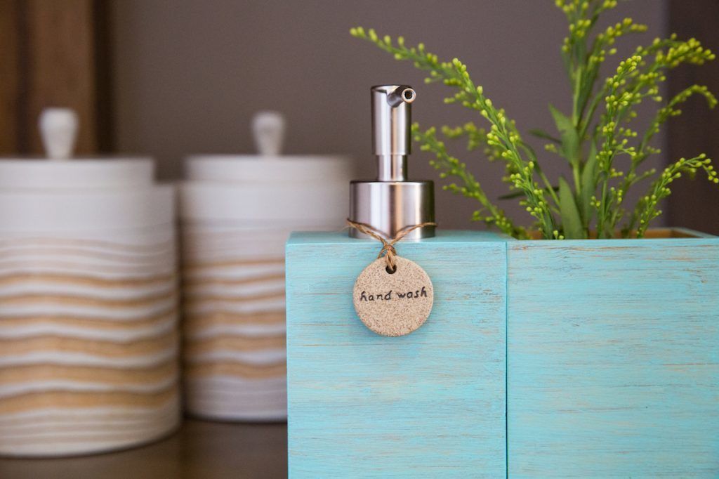 Un distributeur de savon liquide pour les mains, posé sur un bloc de bois, avec une étiquette indiquant « savon pour les mains ».