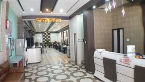 Un vestíbulo de hotel con mostrador de recepción, mostradores de registro, piso estampado y una zona de espera con mesas y sillas.